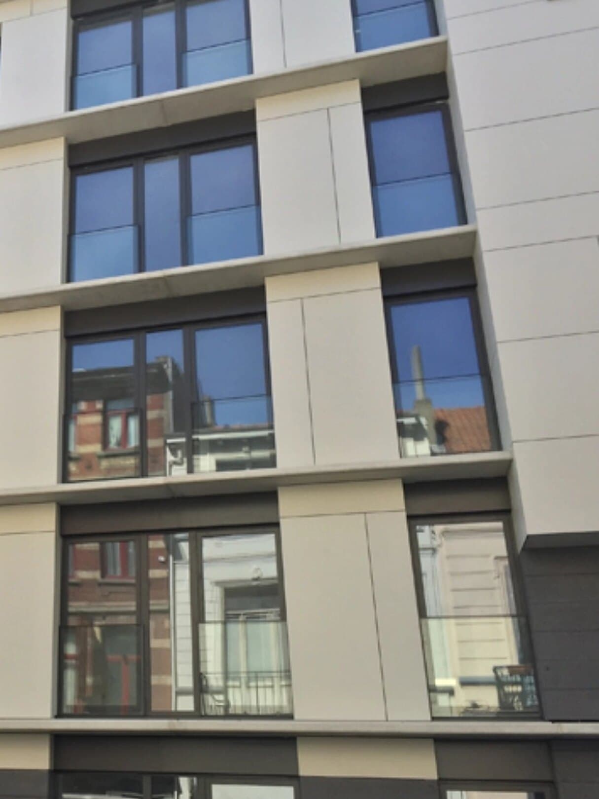 Façade vitrée posée par S.O. Project à Bruxelles, les maisons anciennes d'en face se reflétant dans les châssis